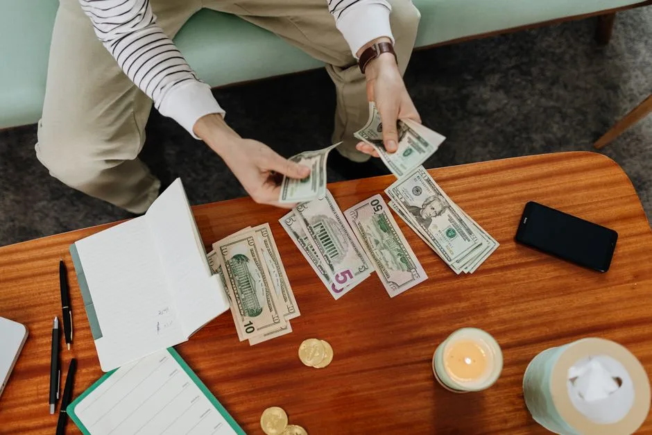 A person sitting and counting various US dollar bills at a table indoors.
