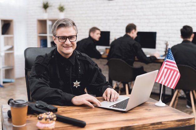 A police officer works for a laptop in a police station.