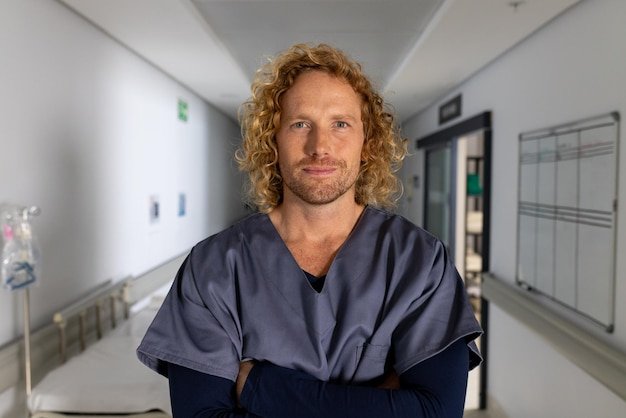 Portrait of happy caucasian male doctor wearing scrubs in corridor at hospital