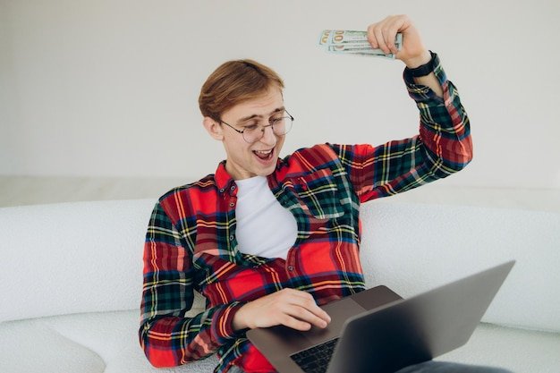 Portrait lucky handsome rich guy entrepreneur got his first money selling or invest into company shaking hand with dollars big sum of cash holding laptop and triumphing