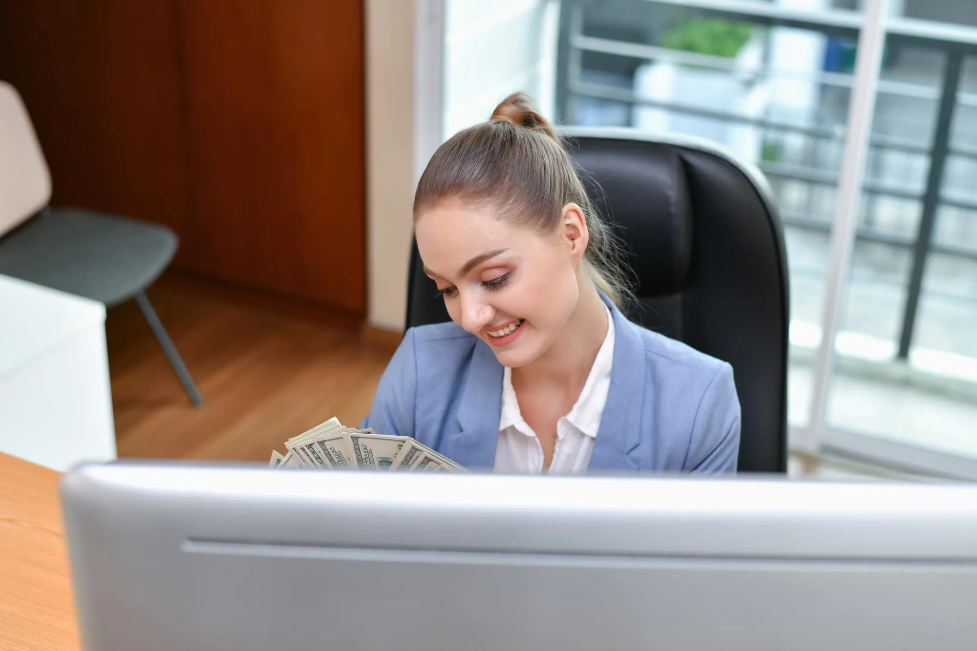 Portrait of smiling businesswoman holding paper currency while sitting at desk in office