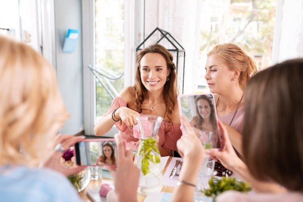 Posing for photo. Beaming dark-haired woman feeling memorable while posing for photo sitting in bakery