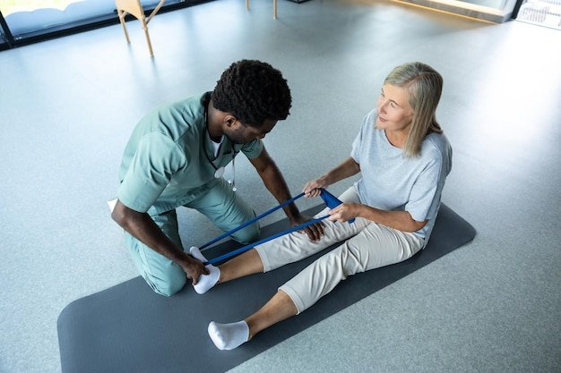 Professional male physiotherapist helping woman with leg injury stretching using resistance band