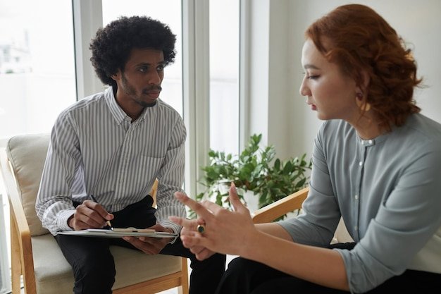 Psychologist taking notes in document when listening to client describing her problem