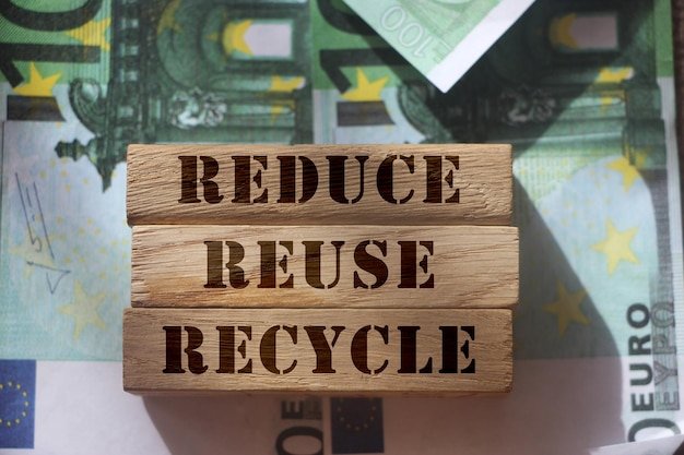 Reduce reuse and recycle words on wooden blocks laying on banknotes of 100 Euro value Saving resources ecology concept
