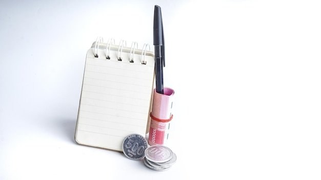 Rolled Indonesian Money 100 thousand rupiah with notebook pen and coins Selective Focus Concept