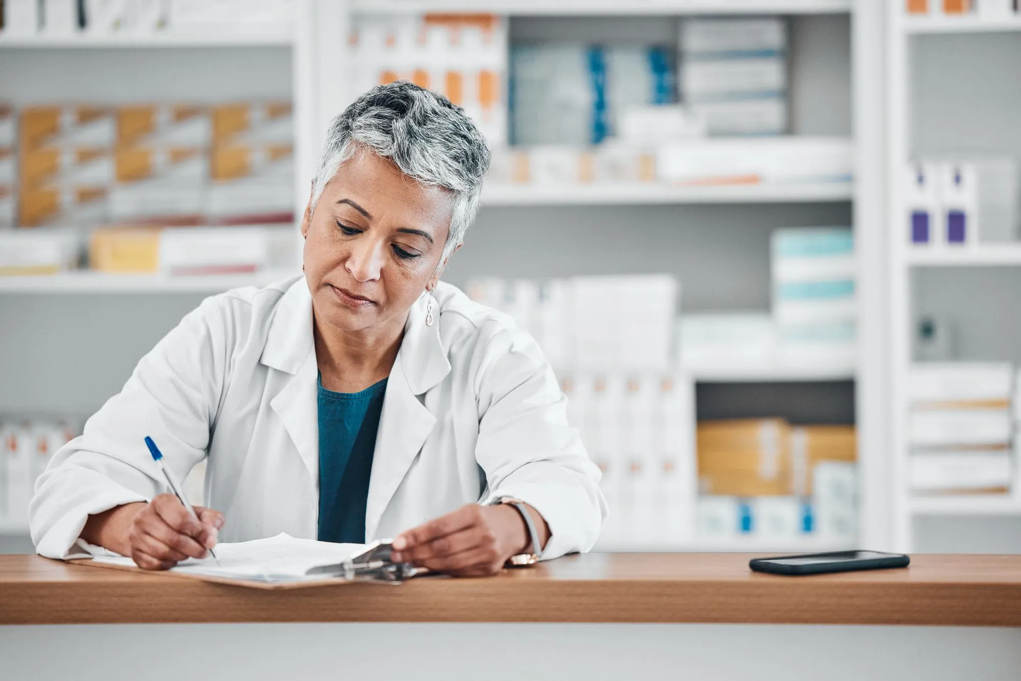 Senior woman pharmacist writing and paper data of pharmacy stock or insurance documents Healthcare doctor and elderly female wellness consultant with store logistics research about shop products