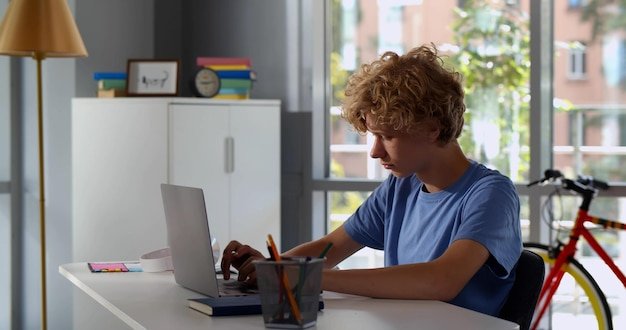 Side view of pupil boy using typing laptop computer doing online lesson