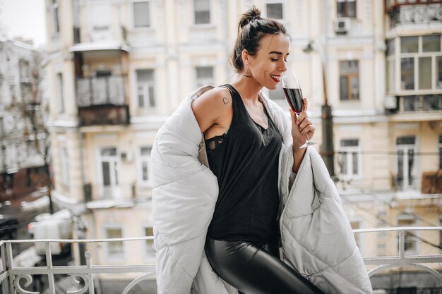 Side view of smiling woman with wineglass wearing blanket while standing at balcony during winter