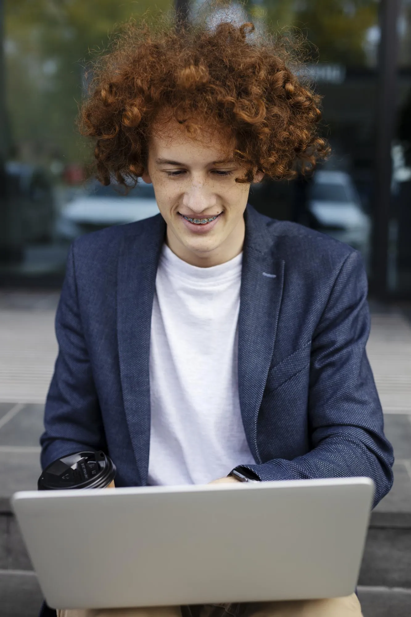 Smiling attractive man using laptop outdoors Successful programmer sitting near modern office