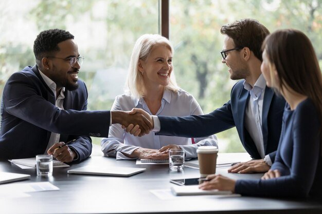 Smiling diverse businesspeople shake hands get acquainted greeting at team meeting in office Happy multiracial male colleagues employees handshake at briefing with coworkers Acquaintance concept
