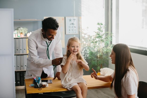 Smiling pediatrician with stethoscope checking little girls lungs