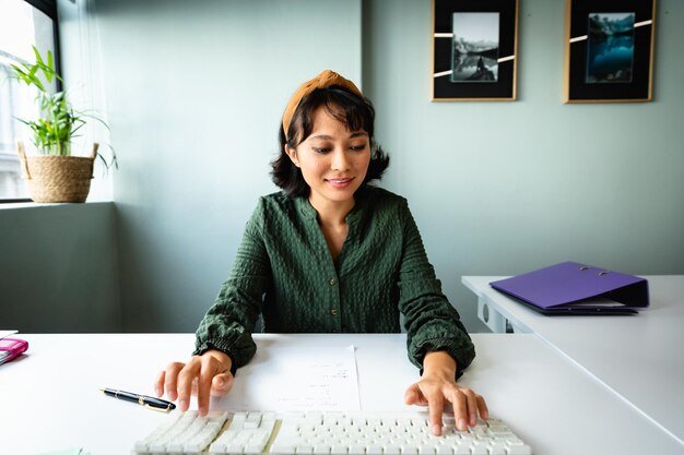 Smiling young asian creative businesswoman using computer keyboard at desk in office