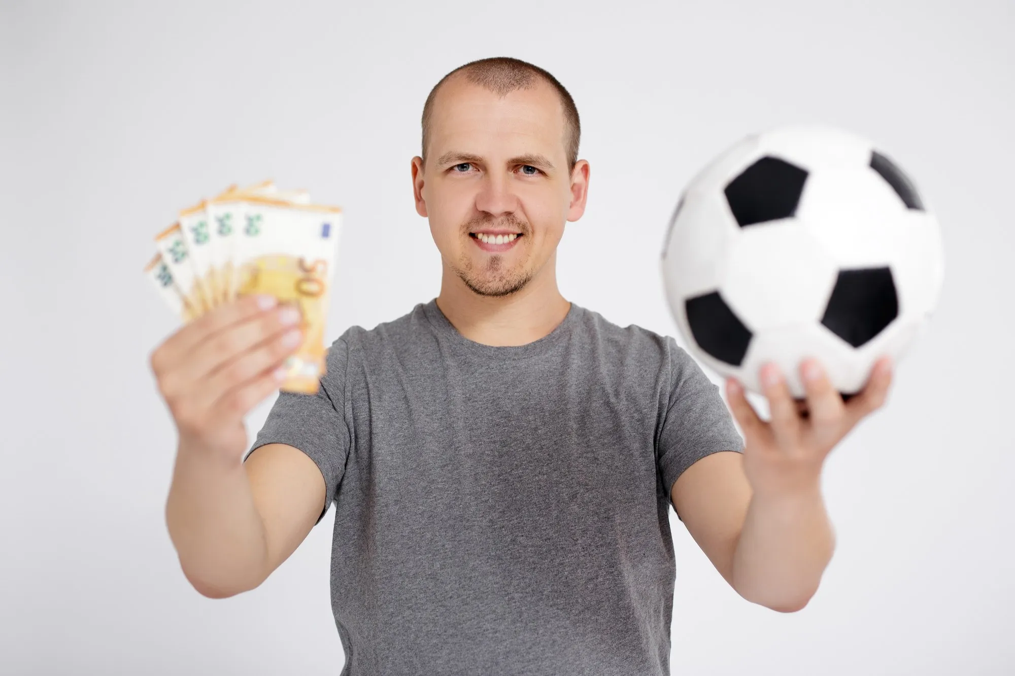 Sport, betting, success, win and money concept - cheerful young man with euro money and soccer ball posing over grey background