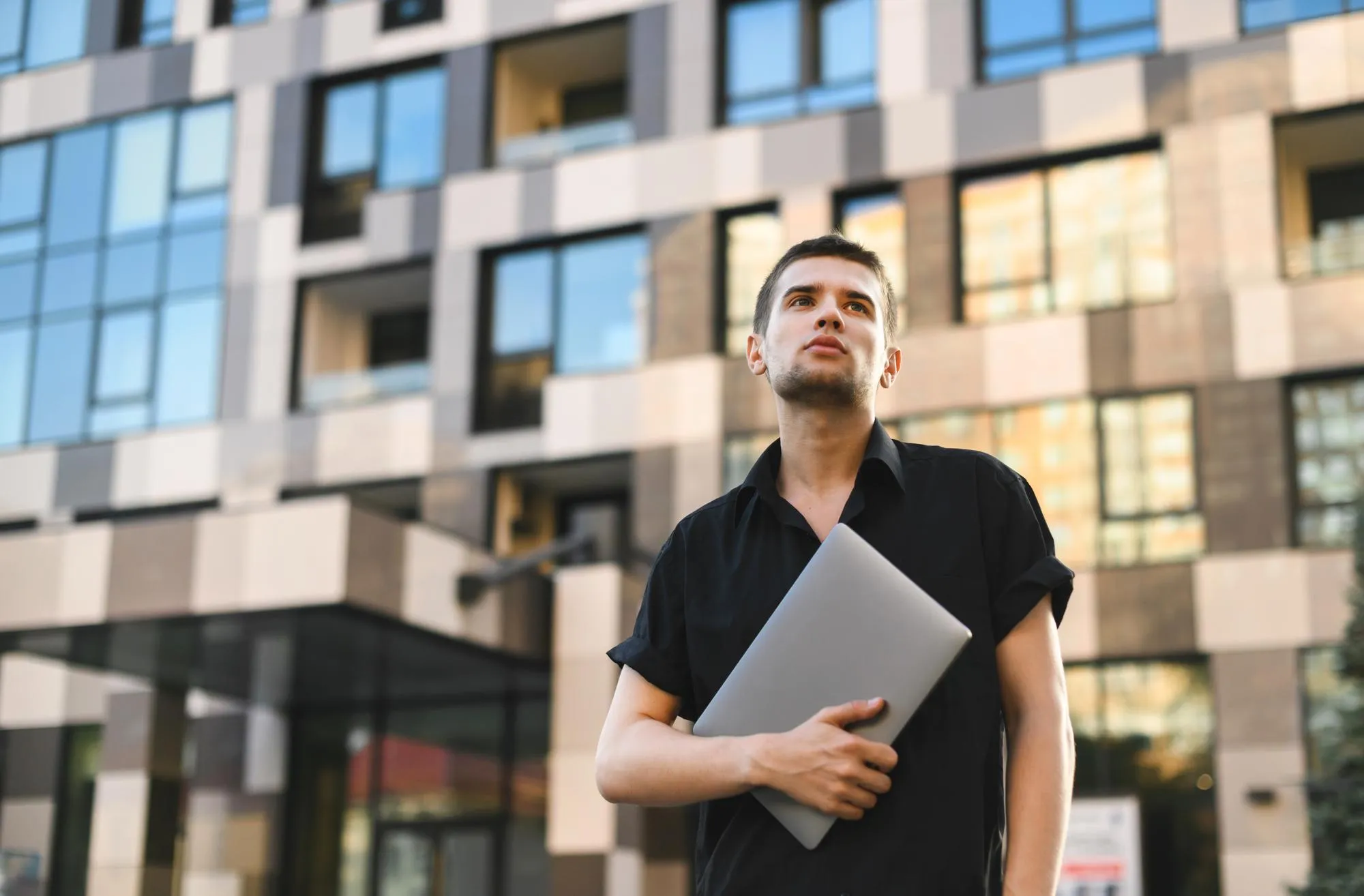 Street portrait of a fashionable man holding a laptop wearing a black shirt