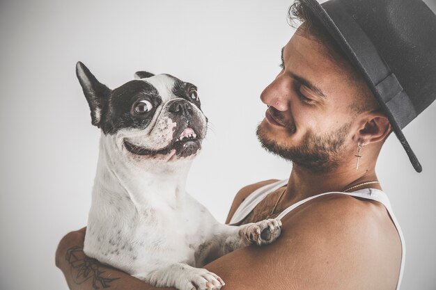 Tattooed boy with piercings with French Bulldog dog in his arms on white background