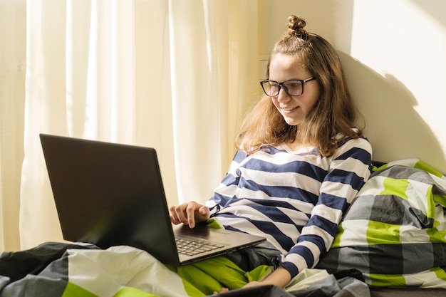 Teenage girl is studying at home uses laptop in bed