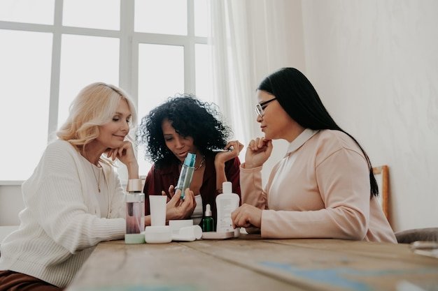 Three mature women examining beauty products while sitting at the desk together