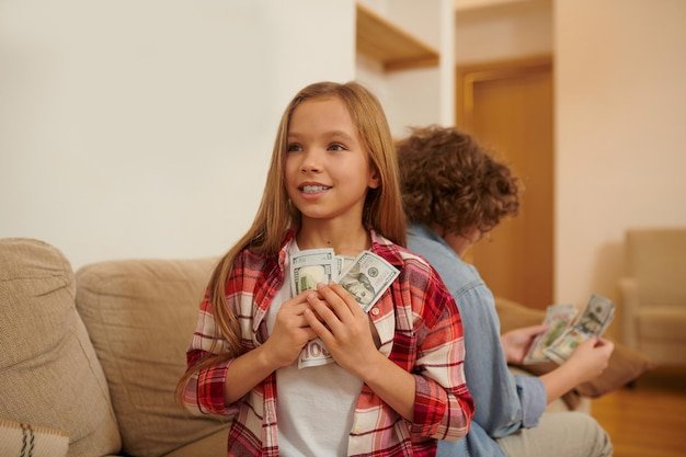 Two teens sitting on the sofa and holding dollars in hands