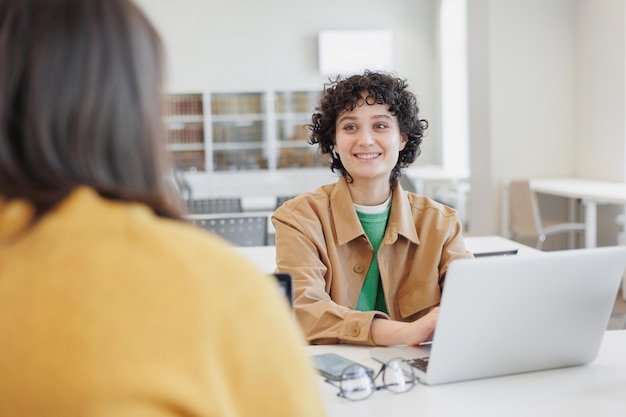 Two women in library or coworking are sitting opposite each other working on laptop