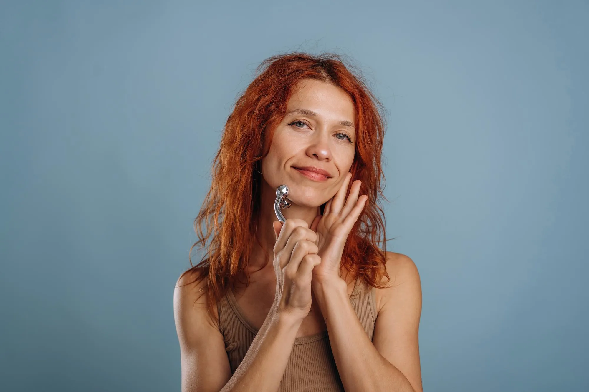 Using massager to take care of face skin Woman is in the studio against background