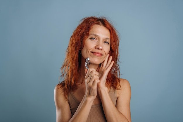 Using massager to take care of face skin Woman is in the studio against background
