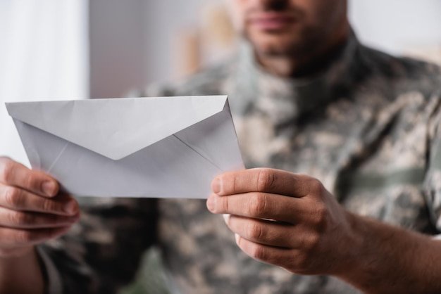 White envelope in hands of military man on blurred background