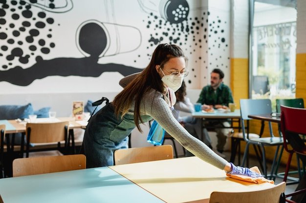 Woman working as waitress sanitizing and wiping table in restaurant