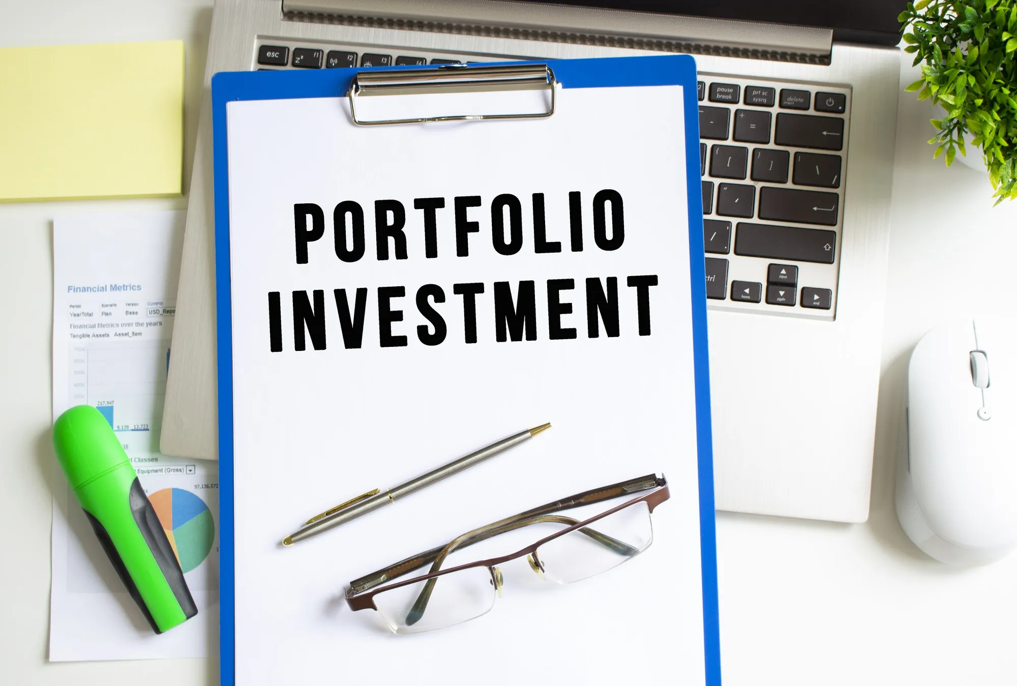 Workplace with laptop, folder, stationery and graph on the table. The folder with the text PORTFOLIO INVESTMENT lies on top of the laptop. Business concept.