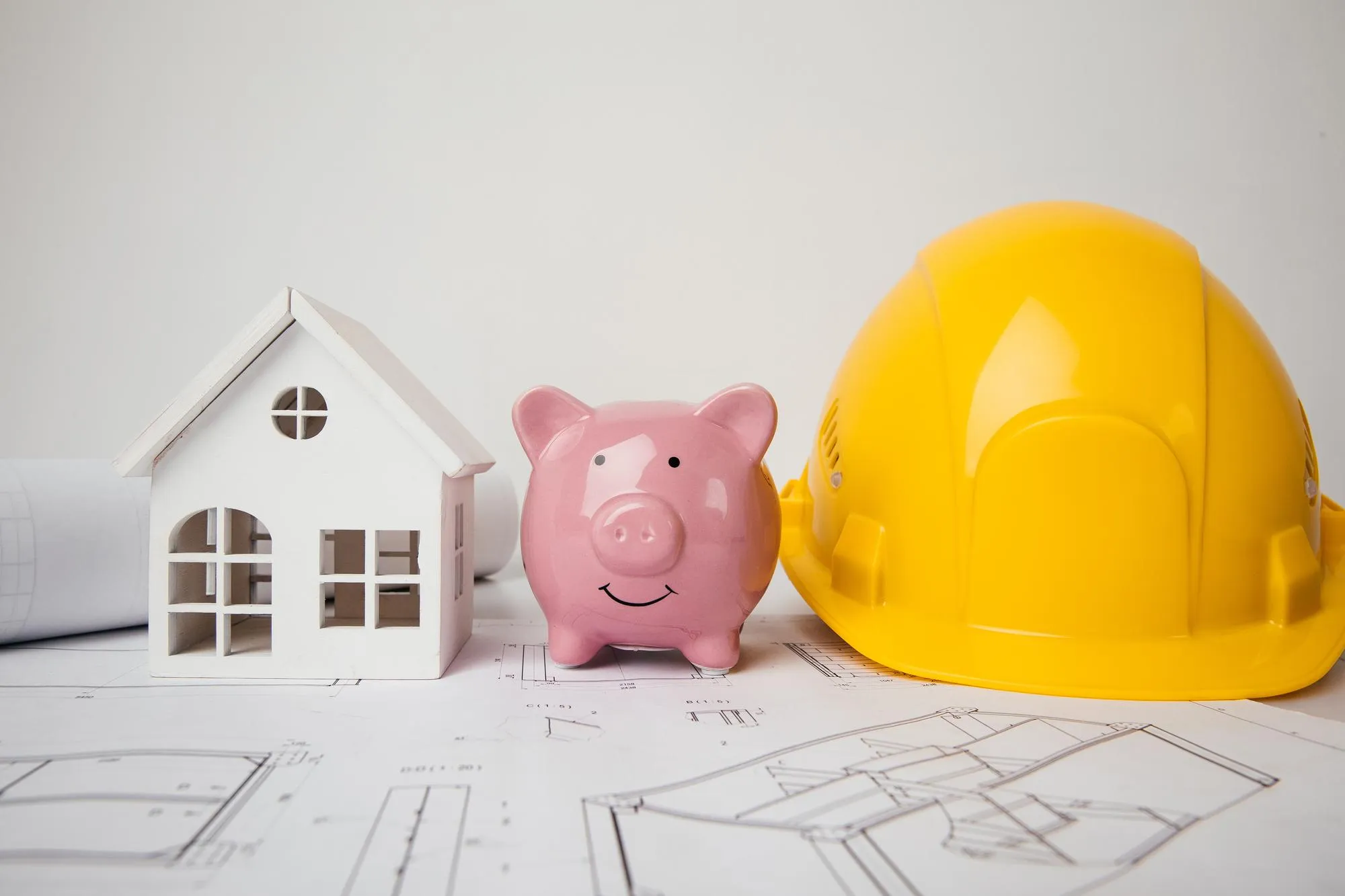 Yellow helmet piggy bank and model of house on drawings