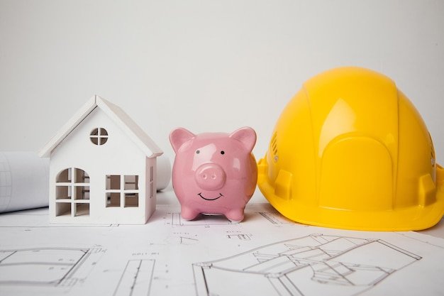 Yellow helmet piggy bank and model of house on drawings