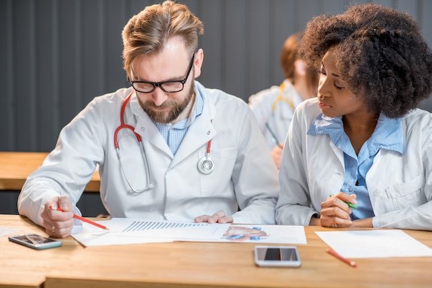 Young african student cheating on medical exam sitting with male student at the desk in the classroom
