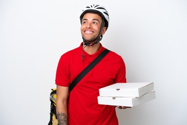 Young Brazilian man with thermal backpack isolated on white background thinking an idea while looking up