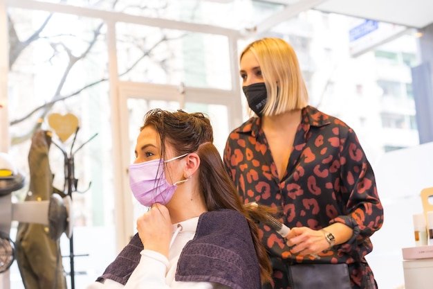 Young hairdresser with face protection mask performing a hairstyle to the client Security measures in the Covid19 pandemic a new normal