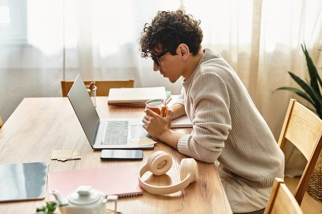 Young man working intently at a wooden table with a laptop and a drink