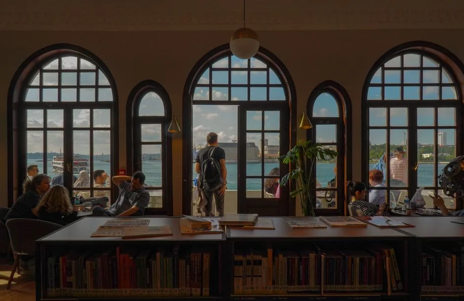 Café interior with people relaxing and a stunning view of Istanbul's waterfront through arched windows.