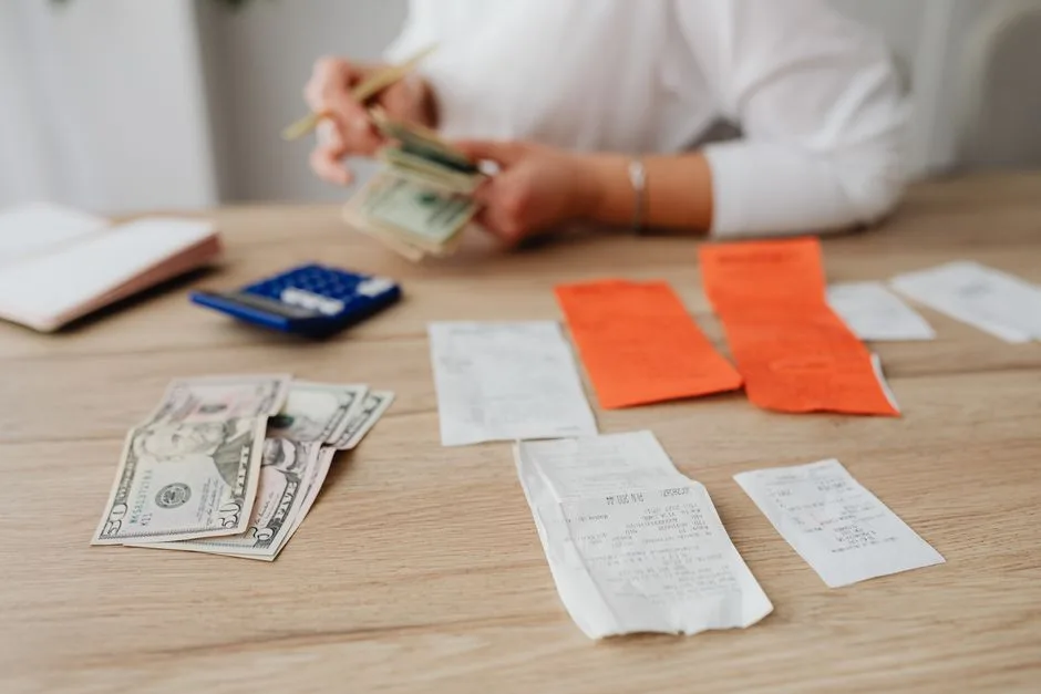 A person using a calculator and cash to plan a household budget.