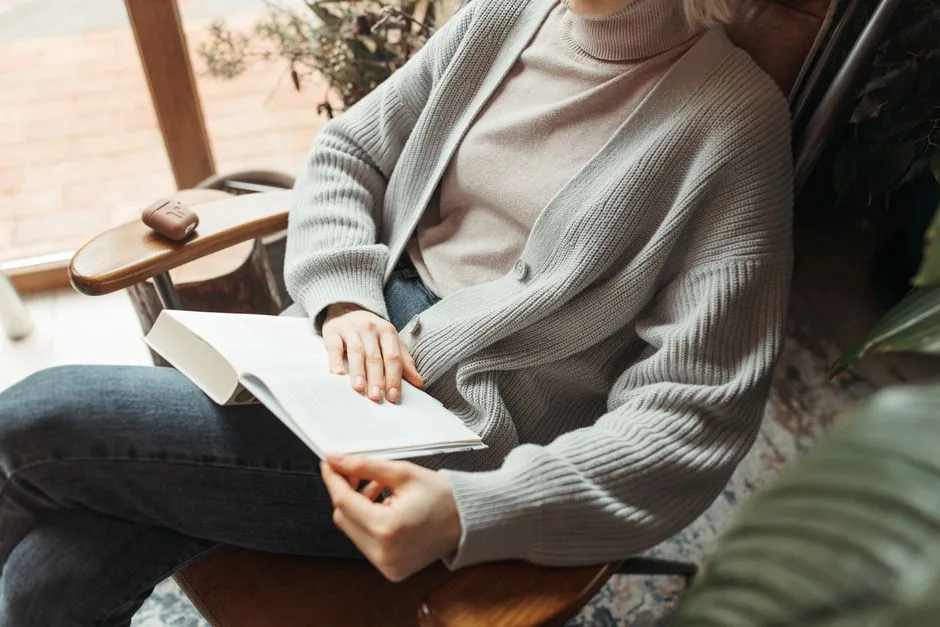 Woman relaxing indoors, reading a book in a cozy armchair. Perfect for lifestyle and relaxation themes.