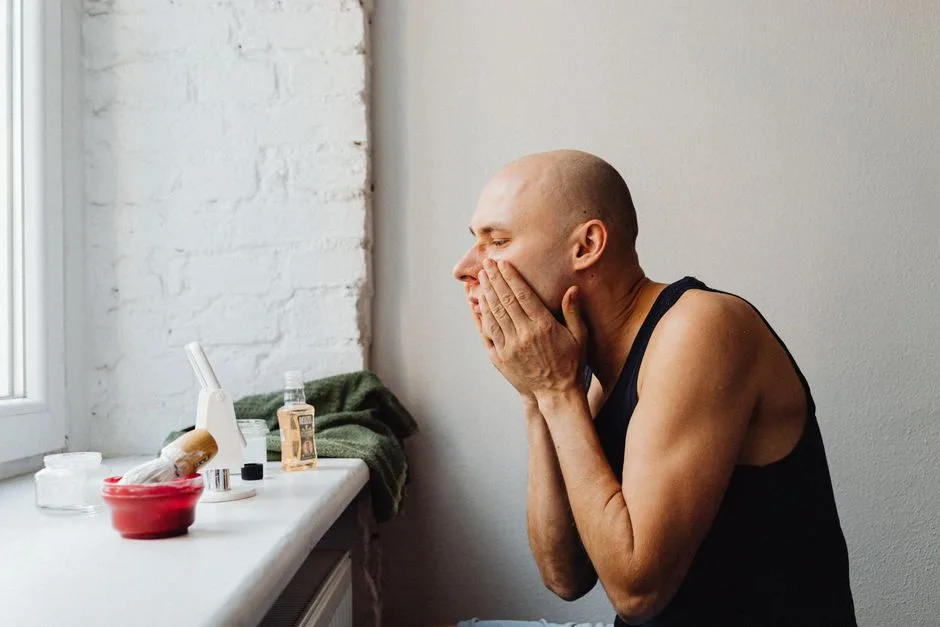 A man applies skincare in a natural-lit bathroom, reflecting self-care and grooming habits.