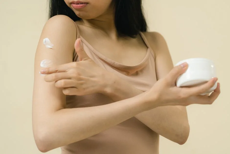 A woman applies moisturizing cream to her arm, focusing on skincare and self-care rituals indoors.