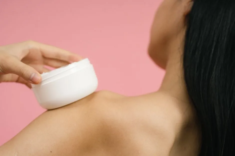 Close-up of a woman applying cosmetic cream to shoulder. Ideal for skincare and beauty themes.