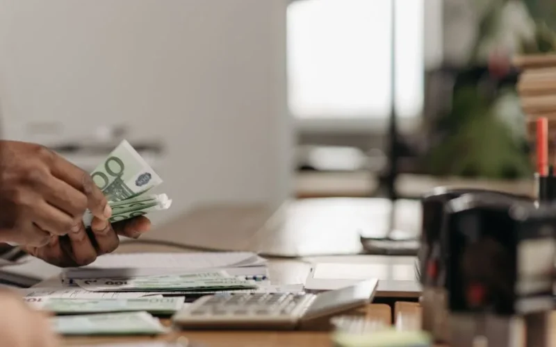 Close-up of hands counting euro bills at an office desk with a calculator.
