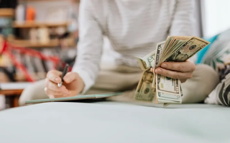 Individual counting money with pen in hand inside a cozy room setting.