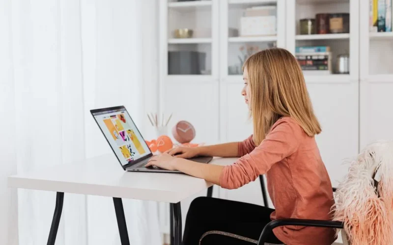 Young girl focused on a laptop while sitting at a desk in a cozy home interior.
