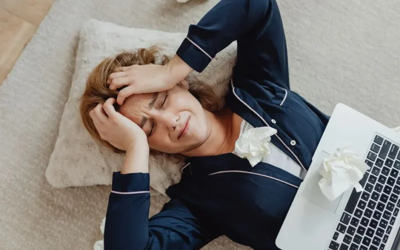 Overhead view of a frustrated woman in loungewear with a laptop and crumpled papers, facing remote work stress.