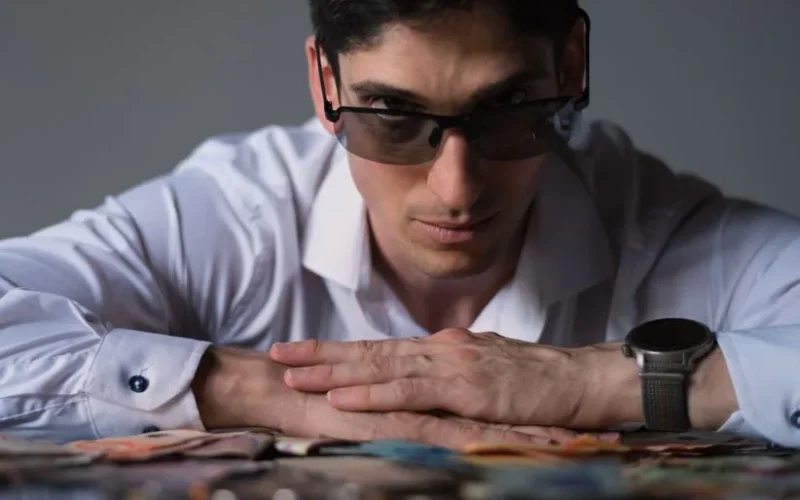 Man in sunglasses with diverse currency, exuding confidence and wealth