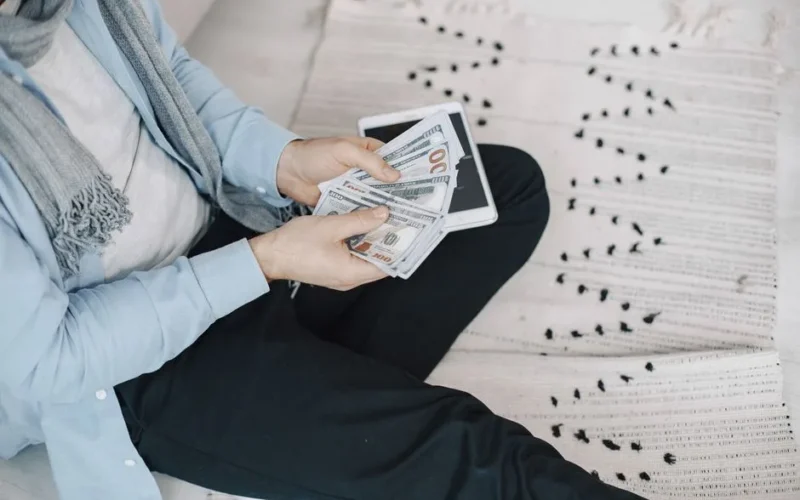 Close-up of adult counting cash with a tablet indoors, symbolizing finance and technology.