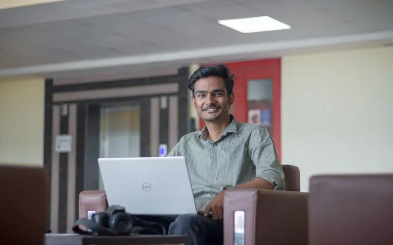 Smiling young man working on a laptop indoors, representing modern freelance lifestyle.