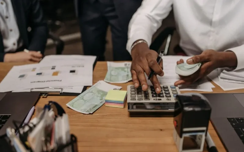 Professional setting with people handling cash and calculations using a calculator at a desk.