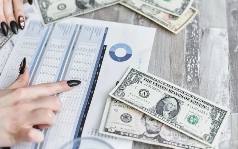 Close-up of hands analyzing financial document with US dollar bills on table.